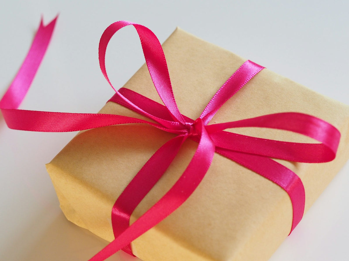 An elegantly wrapped gift box with a pink ribbon, evoking the care of choosing a fragrance gift