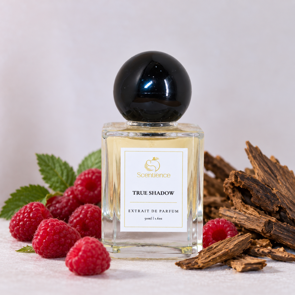 Scentience True Shadow extrait de parfum 50ml bottle beside raspberries and agarwood chips on a white background